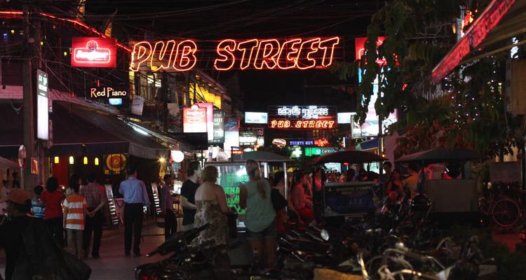 Enseigne de Pub Street éclairée au néon au-dessus d'une scène nocturne animée avec des touristes et des tuk-tuks à Siem Reap.
