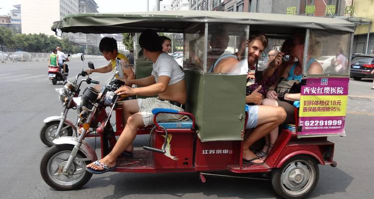 Groupe de voyageurs dans un pousse-pousse motorisé ouvert circulant dans une rue animée d'une ville asiatique.