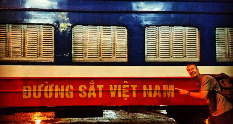 Voyageur pointant vers un wagon de chemin de fer vietnamien avec des lettres jaunes vives dans une gare de nuit.