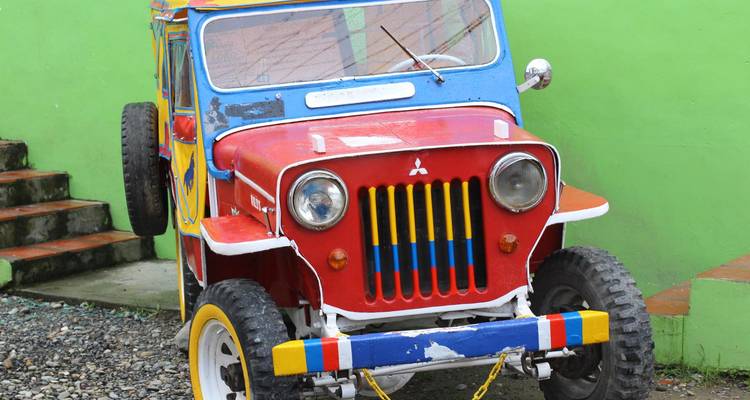 Jeep Willys coloré restauré garé contre un mur vert vif dans la région caféière de Colombie.