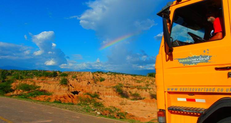 Camion d'expédition garé à côté d'un paysage désertique coloré avec un arc-en-ciel tenu au-dessus.