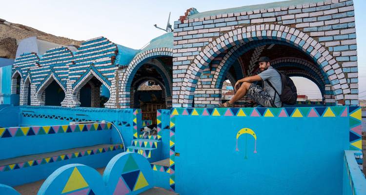 Un voyageur se perche sur l'arche à motifs d'un bâtiment nubien bleu aux couleurs vives décoré de motifs géométriques colorés.
