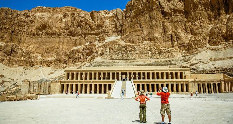 Le grand temple en terrasses d'Hatchepsout se dresse contre les falaises escarpées du désert tandis que les touristes photographient la façade monumentale.