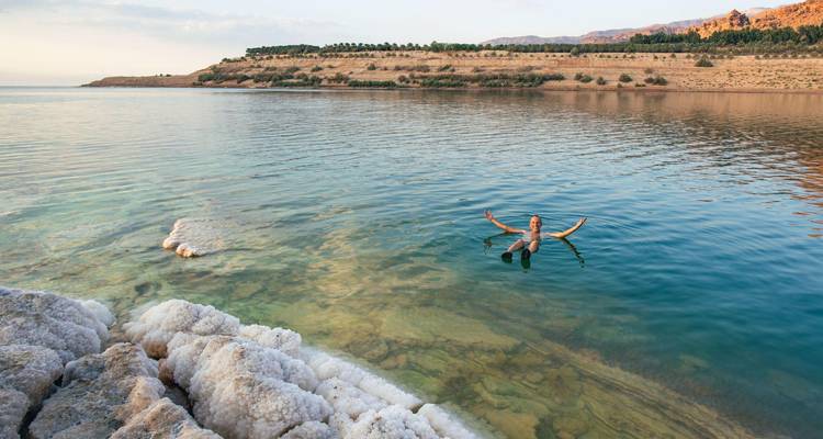 Un nageur flotte sans effort dans les eaux turquoise de la mer Morte près des formations côtières incrustées de sel.