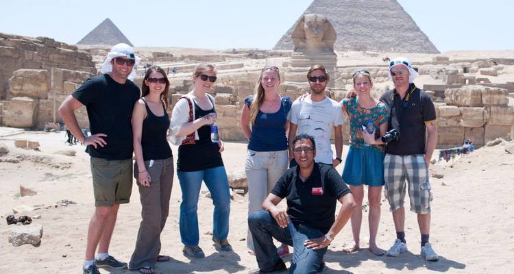 Un groupe de touristes pose en souriant devant le Sphinx et les Grandes Pyramides lors d'une journée ensoleillée dans le désert.