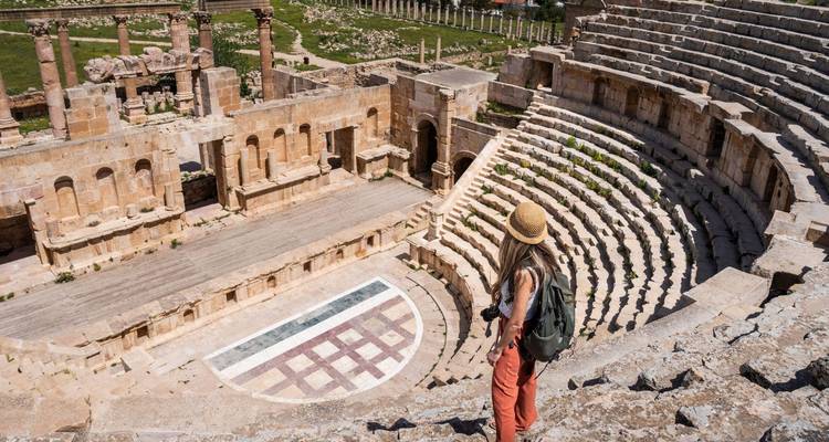 Surplombant un grand amphithéâtre romain, un voyageur solitaire admire les anciens sièges de pierre et la scène en contrebas.