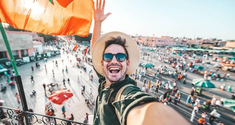 Voyageur excité prenant un selfie au-dessus de la place animée Jemaa el-Fnaa en agitant le drapeau marocain.