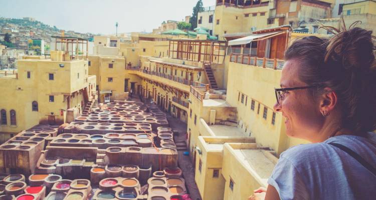 Voyageuse observant les fosses de teinture colorées de la tannerie de Fès depuis un balcon.