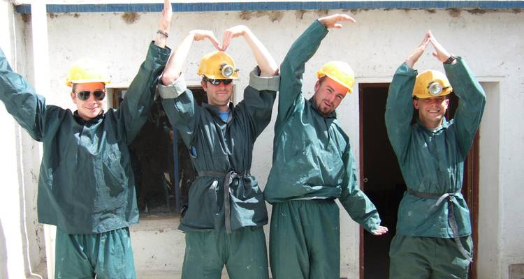Vier reizigers in groene mijnoveralls en gele helmen poseren speels terwijl ze hartvormige figuren maken met hun armen.