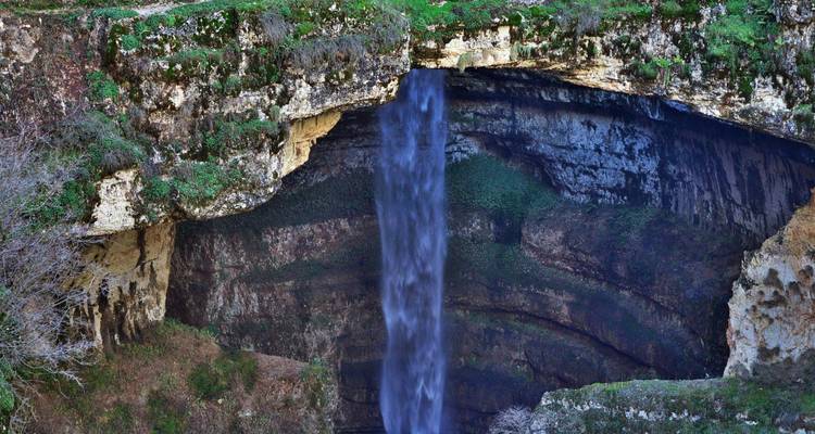 Grande cascade plongeant d'une falaise calcaire dans une gorge caverneuse entourée de verdure.