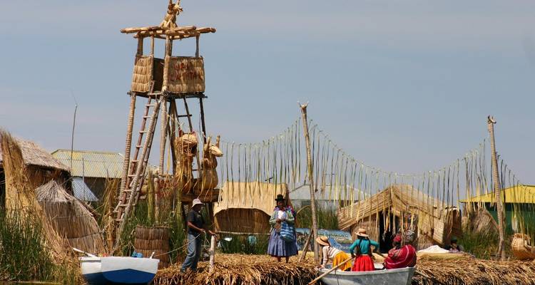 Traditionele rieteilanden hebben uitkijktorens en boten terwijl lokale bewoners in felgekleurde kleding hun dagelijks leven leiden.