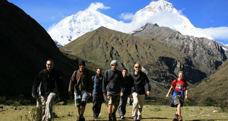 Groep trekkers stapt door alpine weide met besneeuwde Andes toppen die hoog oprijzen erachter.