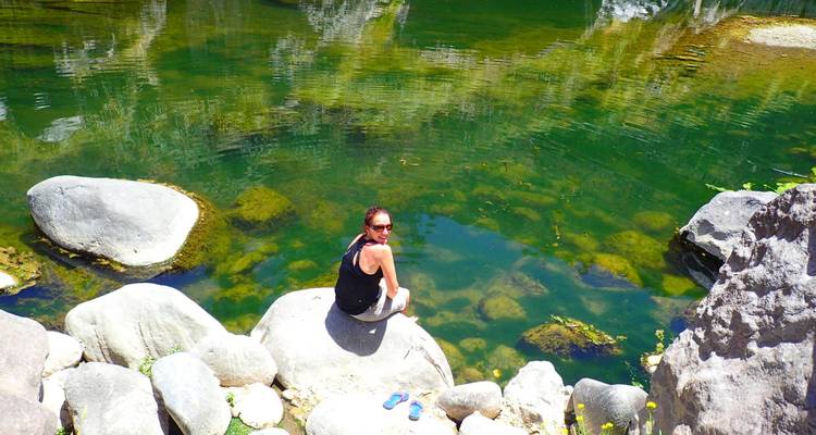 Reiziger rust op een rotsblok naast een heldere groene natuurlijke poel omringd door rotswanden.