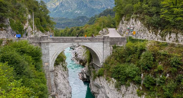 Puente histórico de piedra sobre un río turquesa en una zona boscosa.