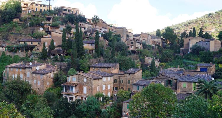 Pueblo rústico en la ladera con casas de piedra densamente agrupadas y vegetación exuberante.