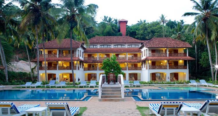 Bâtiment de complexe hôtelier avec une piscine, entouré de palmiers.