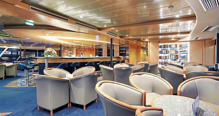 Comfortabele loungeruimte op een schip met fauteuils, bar en boekenkasten.