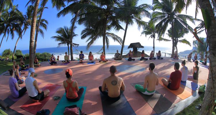 Groepsyogasessie op een terras aan het strand met uitzicht op de oceaan.