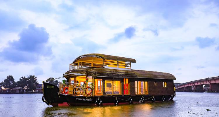 A lit-up houseboat on still water during twilight.