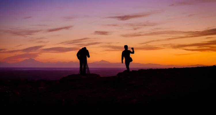 Twee gesilhouetteerde figuren op een rotsachtig landschap tijdens zonsondergang of zonsopgang.