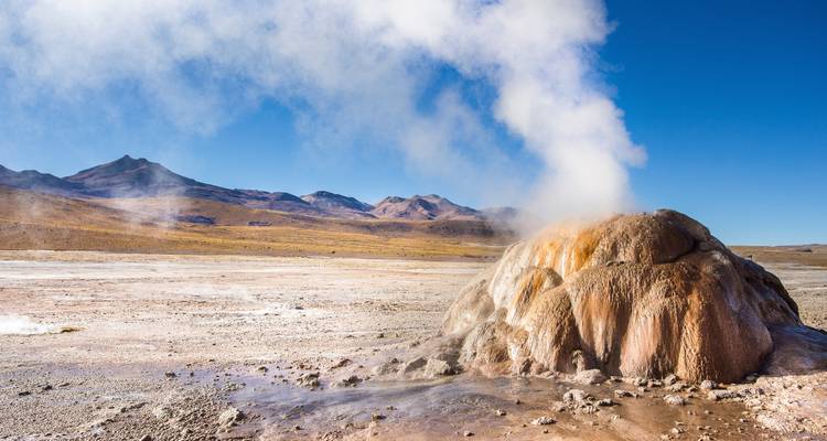 Geothermische bron met opstijgende stoom in een woestijnlandschap.