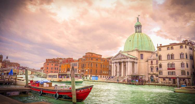 Hermosa escena de canal con una cúpula y cielo vibrante, gente paseando en botes en Venecia.