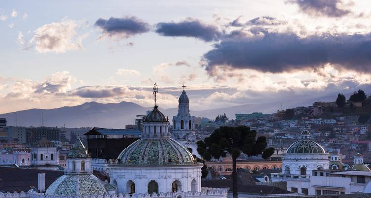 Colonial domes and rooftops of Quito’s historic centre set against a dramatic sunset sky and distant mountains