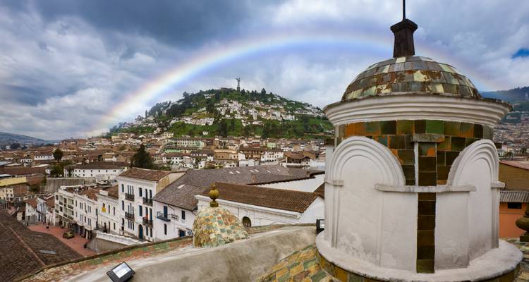 Rainbow arcing over Quito’s hillside and colonial rooftops with the Virgin of El Panecillo statue visible on the summit