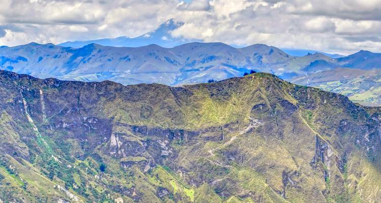 High-altitude ridgeline with layered rock faces and distant blue mountains under a partly cloudy sky