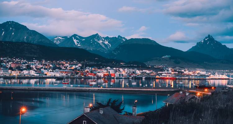 Paysage urbain au crépuscule avec montagnes et reflets sur l'eau.