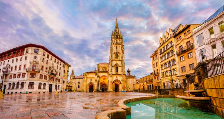 Dramatischer Sonnenaufgangshimmel über der Kathedrale von Oviedo spiegelt sich in einem nassen Platz mit Brunnen wider