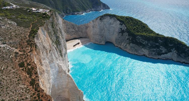 Una vista aérea dramática de la playa Navagio (del Naufragio) donde el agua turquesa se encuentra con imponentes acantilados blancos y una cala arenosa oculta en Zakynthos.