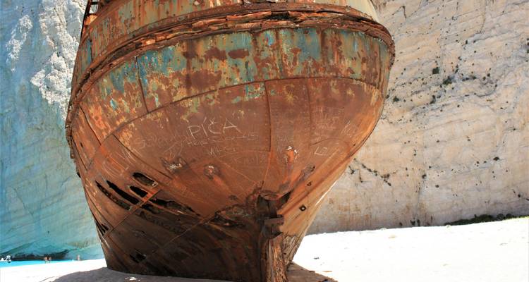 Primer plano del casco oxidado del famoso naufragio que descansa en una playa de arena blanca bajo acantilados escarpados de piedra caliza.