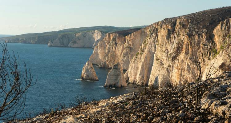 Acantilados blancos escarpados caen hacia aguas azul profundo a lo largo de una costa agreste bajo la luz del final de la tarde.