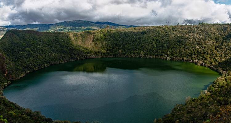 Kratersee umgeben von üppiger Vegetation und Wolken.