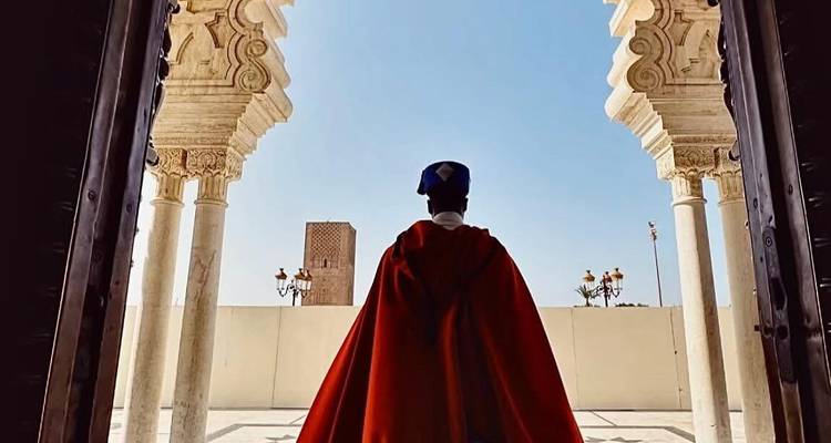 Wächter in traditioneller Kleidung steht zwischen verzierten Steinsäulen.