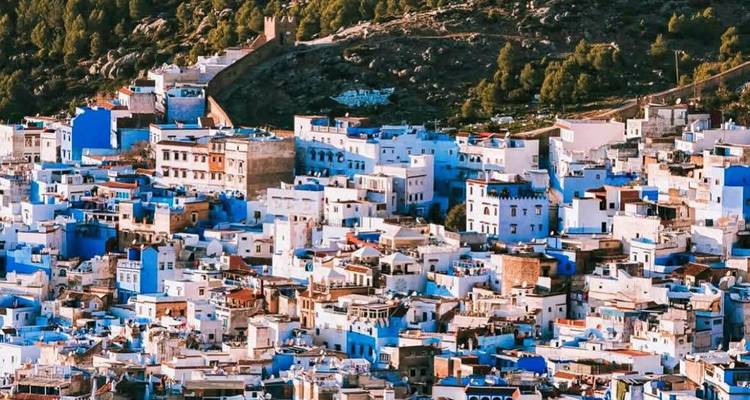 Malerischer Blick auf eine blau bemalte Stadt vor einer bergigen Kulisse.