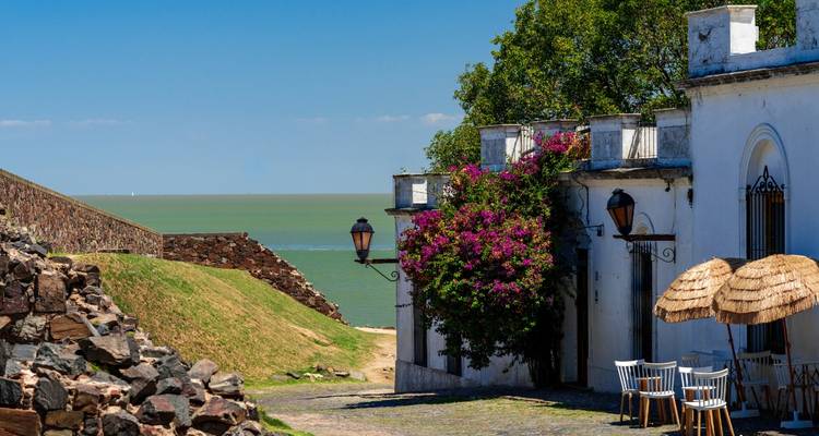 Rue pavée pittoresque avec des bâtiments de style colonial et des fleurs éclatantes donnant sur la rivière.