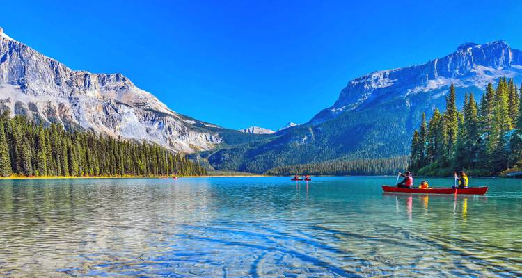 Lac alpin turquoise encadré par des montagnes escarpées et des forêts de pins avec des canoéistes qui glissent sur une eau calme.