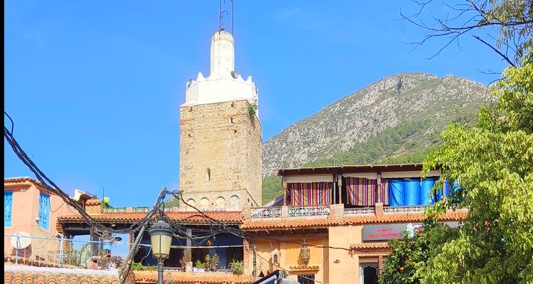 Bâtiment historique avec une tour blanche et un paysage montagneux en arrière-plan.