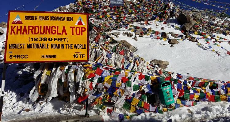 Panneau de Khardungla Top avec drapeaux de prière sur un paysage enneigé.