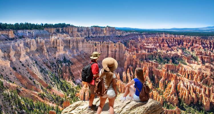 Tres excursionistas disfrutando de una vista dramática del laberinto de chimeneas de hadas naranjas del Cañón Bryce.
