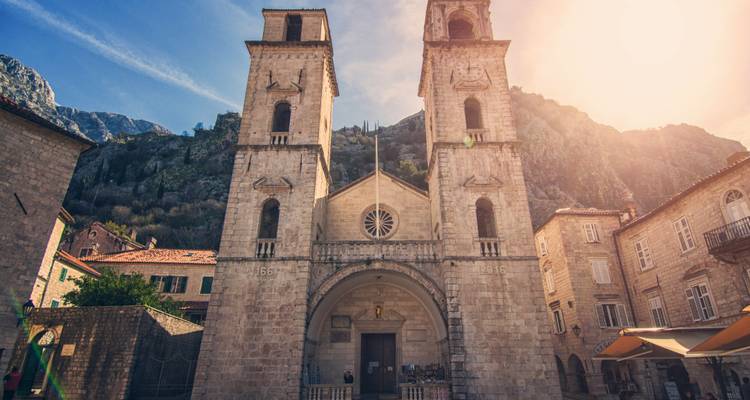 Façade d'église avec deux tours devant une colline rocheuse.
