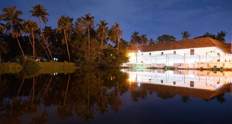 Reflets de bâtiments illuminés et de palmiers sur un plan d'eau la nuit.
