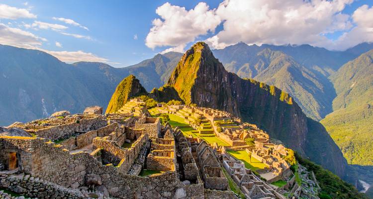 Sonnenbeschienene Steinterrassen von Machu Picchu erstrecken sich zum ikonischen Huayna Picchu-Gipfel unter einem teilweise bewölkten Himmel.