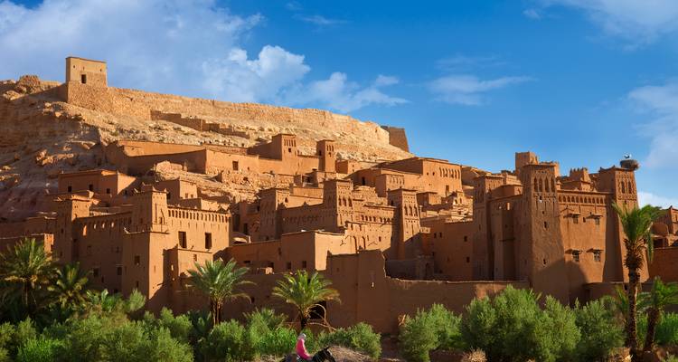 De oude leemstenen stad Ait Benhaddou met blauwe lucht en groene vegetatie.