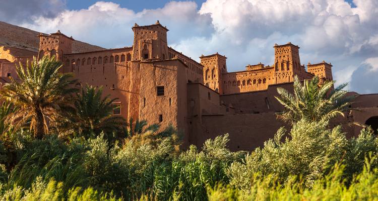 Adembenemend uitzicht op Ait Benhaddou met weelderige begroeiing en dramatische lucht.