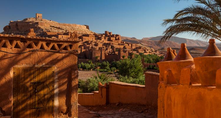 Historische Kasbah in der marokkanischen Wüste, umgeben von Grünflächen unter blauem Himmel.