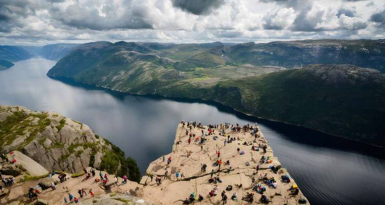 Numerosas personas de pie en el borde de un acantilado con vistas al fiordo.