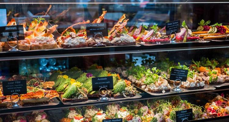 Vitrina con varios sándwiches abiertos en una delicatessen.